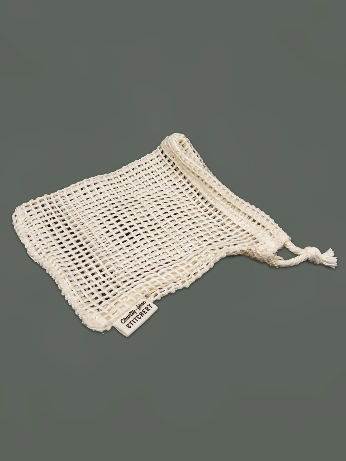 An off-white cotton mesh drawstring soap saver bag with a small woven label reading 'Cruelty-Free Stichery' on a solid dark gray background.