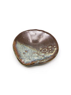 A small organic-shaped ceramic dish with a glossy dark brown glaze and a contrasting light blue and cream metallic-looking pattern on one side, shown on a plain white background.