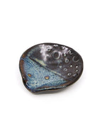 A small organic shaped round ceramic teaspoon or trinket dish with stormy dark brown and blue design