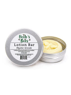 An open silver metal tin of Herb's Bees Lotion Bar in the 'Mystic Woods' scent, showing the pale yellow lotion inside, next to its lid which features a white label.
