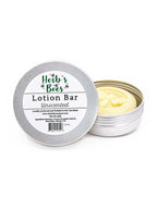 An open round metal tin of Herb's Bees unscented lotion bar next to its lid, which features a white label with green and black text, on a clean white background.