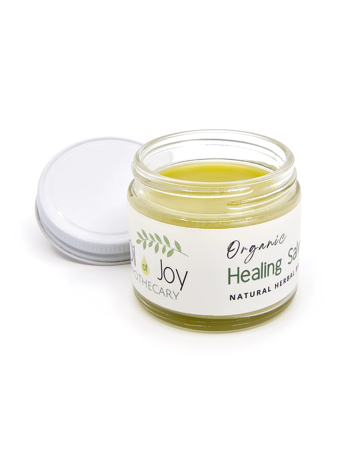 An open glass jar of organic healing salve with its white lid resting beside it on a clean white background. The salve inside is a pale yellow-green, and the label reads 'Organic Healing Salve' by 'Oil of Joy Apothecary'.