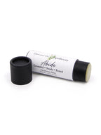 A lip balm tube labeled Abide by Remnant Oil Apothecary, shown with its black cap removed and placed beside the tube on a white background.