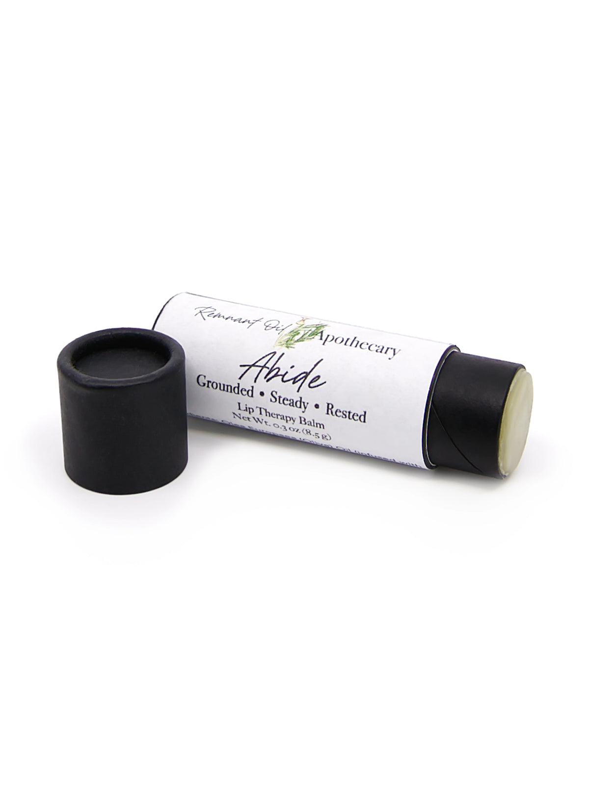 A lip balm tube labeled Abide by Remnant Oil Apothecary, shown with its black cap removed and placed beside the tube on a white background.