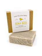 A bar of soap labeled 'THE YELLOW BIRD SOAP BAR' resting in front of its kraft paper packaging box on a white background.